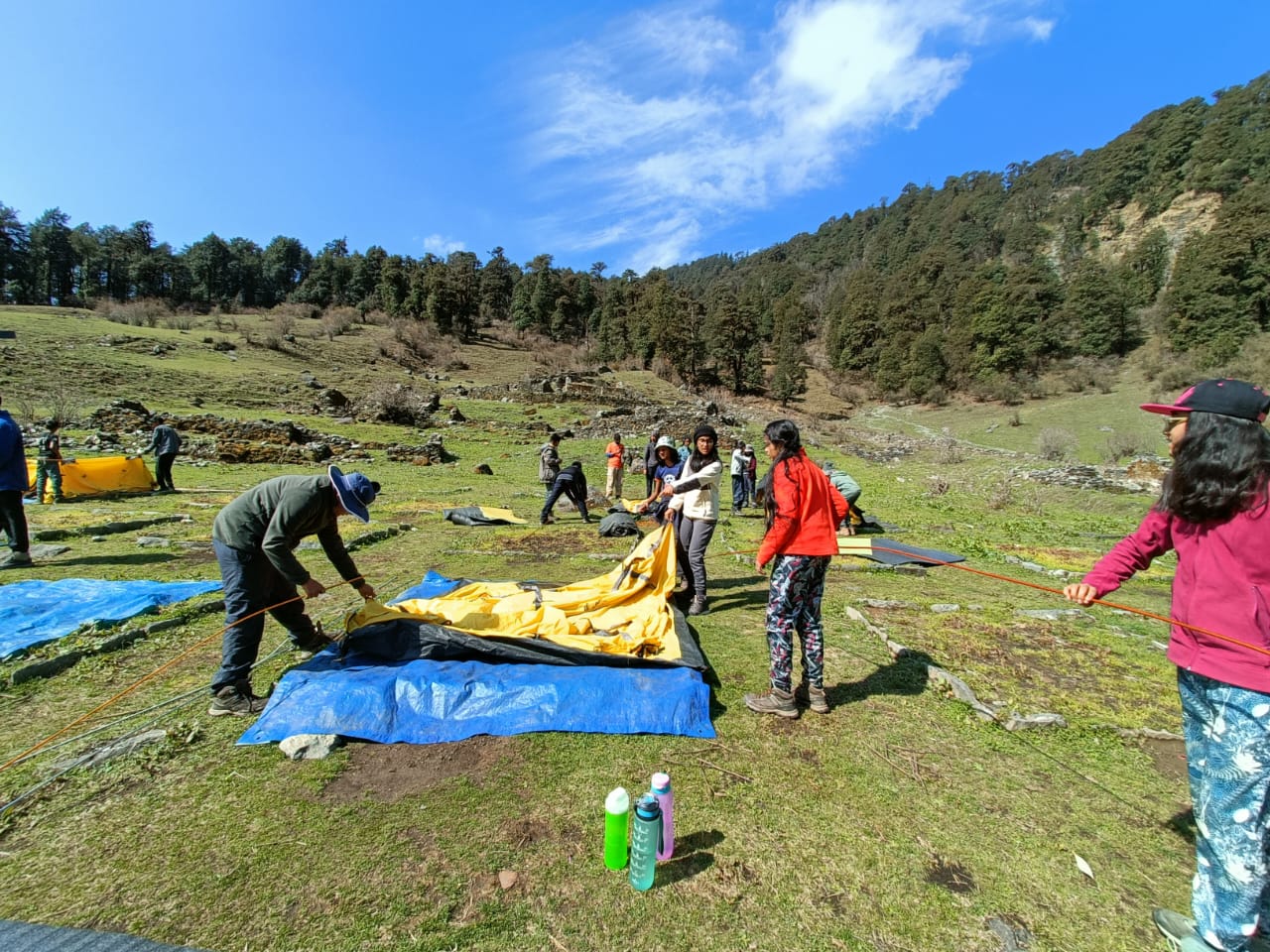 Trekkers working together to pitch a yellow tent on a green meadow campsite